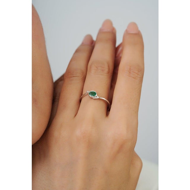 Crafted in 925 sterling silver, this elegant ring features a vibrant 0.40 ct oval-cut emerald accented by 0.04 ct total...