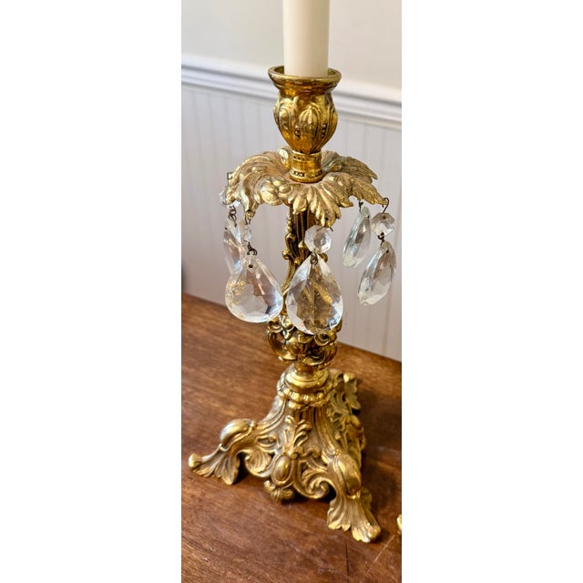 This pair of vintage candle holders are characterized by their elaborate gold colored metalwork and dangling crystal...