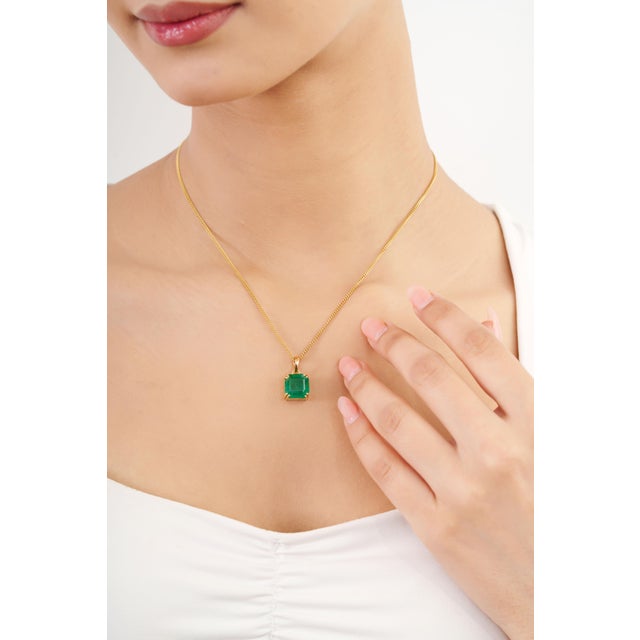 This minimalist solitaire pendant features a 6.06-carat emerald-cut green emerald, set in 14k yellow gold. The center...