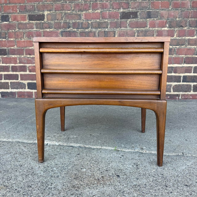 This is a Lane Rhythm walnut nightstand. It features clean simple lines and one large drawer for storage.