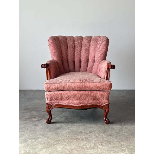 An elegant channel-back armchair with a sculpted, fan-shaped tufted back, scrolled carved wood arms, and cabriole legs in...