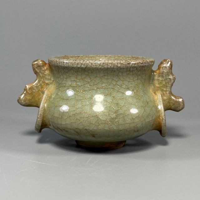 A vintage‑style Chinese Longquan celadon censer, featuring two dragon‑shaped side handles. The surface has natural...