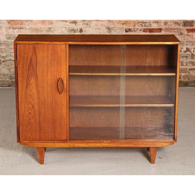 Mid century glass fronted teak bookcase, circa 1960s. A cabinet section and two sliding glass door with adjustable shelves...