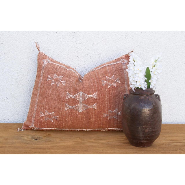 A pair of stacked diamond medallions with wing-like flanking marks anchor this handcrafted Moroccan cactus silk lumbar...