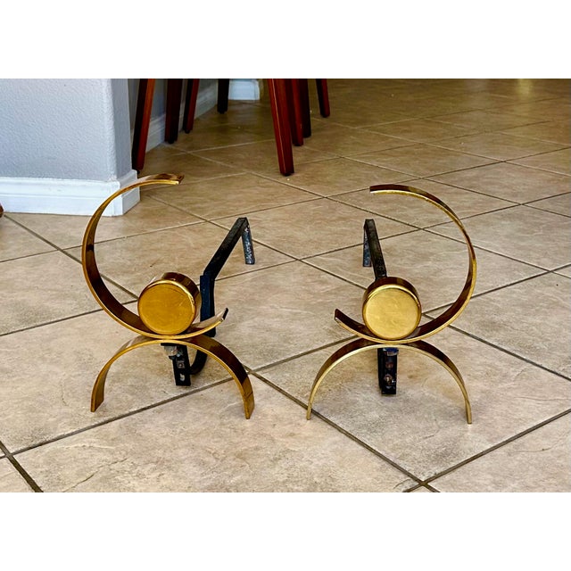 Pair of mid century andirons in mirror image crafted from brass and black iron, attributed to Donald Deskey. Brass has a...