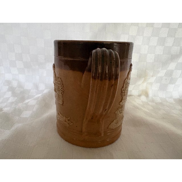 The mug dates to circa 1880. It is made by Dolton lambeth in stoneware featuring a two tone brown glaze adorned with...