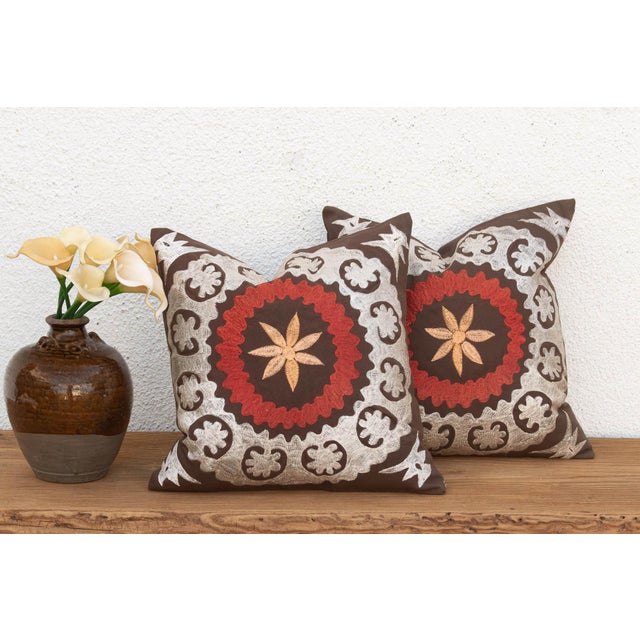 A large floral medallion in raised, hand-embroidered satin stitch anchors the center of this pillow — radiating palmette...