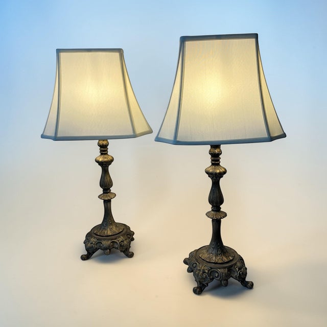 Mid century gilt footed baroque style table lamps. Rectangular cream color shades are included. Lamp mrasured 7.5” square,...