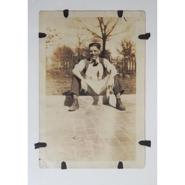 Early 20th century sepia tone silver gelatin snapshot photograph of young man in shop apron taking a break. Unframed,...