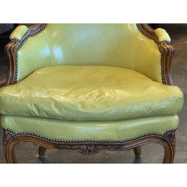 A bergère with a shaped back and upholstered in green leather, outlined with rows of nailhead trim that follow the curves...