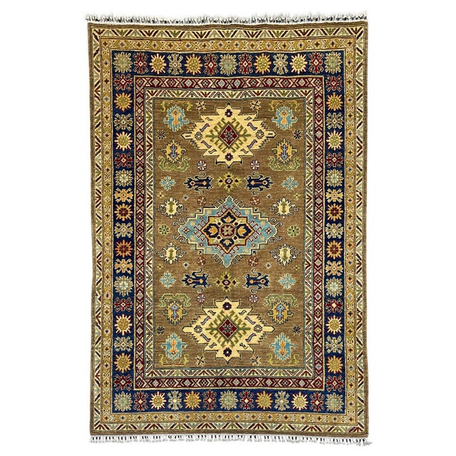 This Kazak-style tribal area rug features three bold medallions across a warm brown field. Light blue, cream, burgundy,...