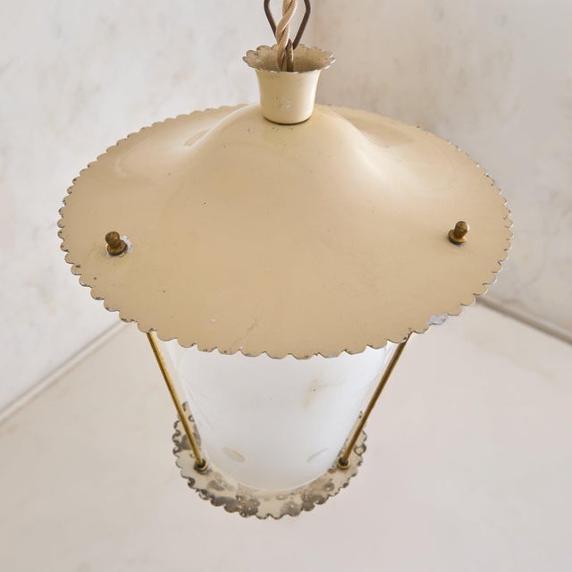 A 1950s Italian lacquered metal lantern pendant with a softly tapered silhouette. The ivory-toned frame descends from a...