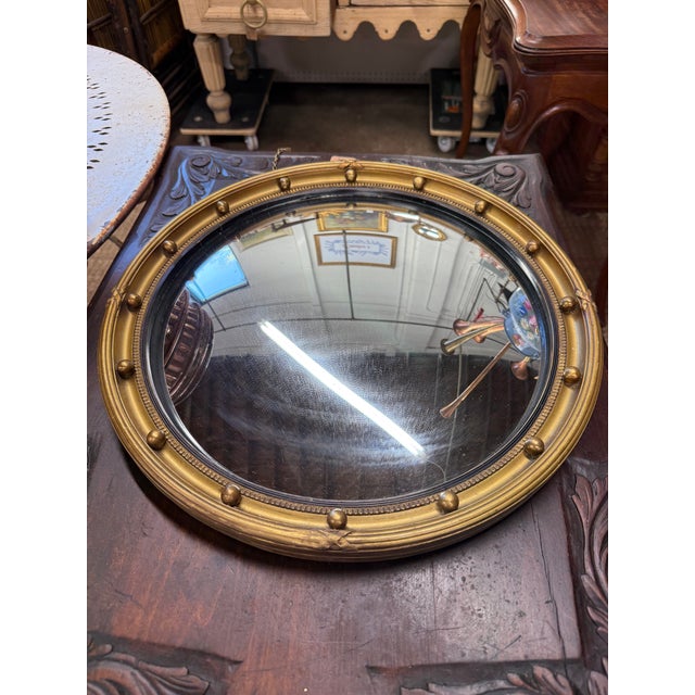 A classic antique English convex “bullseye” mirror dating to the mid-19th century, crafted in the elegant Regency style....