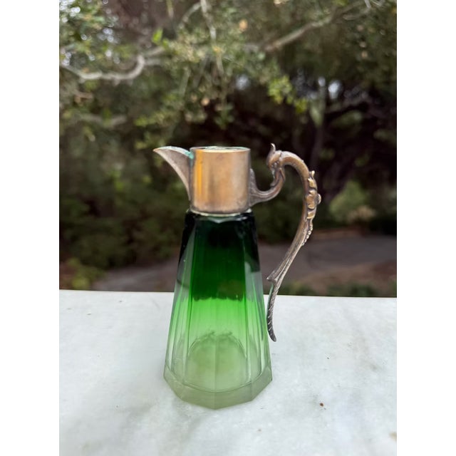 An elegant antique decanter featuring beautifully beveled prism glass in a rich emerald-to-clear gradient with a warm...