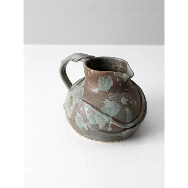This is a vintage studio pottery pitcher. The handmade ewer features a raised ceramic vine design that wraps around the...