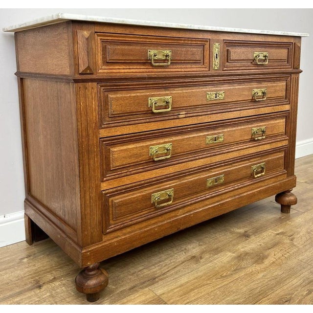 An elegant Antique French chest of drawers in oak, featuring a white marble top, five drawers and decorative metal handles...