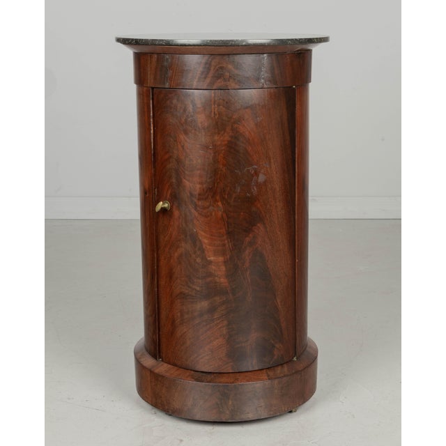 A 19th Century French Empire style circular side table, or nightstand, made of beautifully patterned veneer of mahogany on...