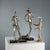 Two sculptures of varying sizes made of rock dust and resin, coated in silver and gold, depicting a man and a woman in...