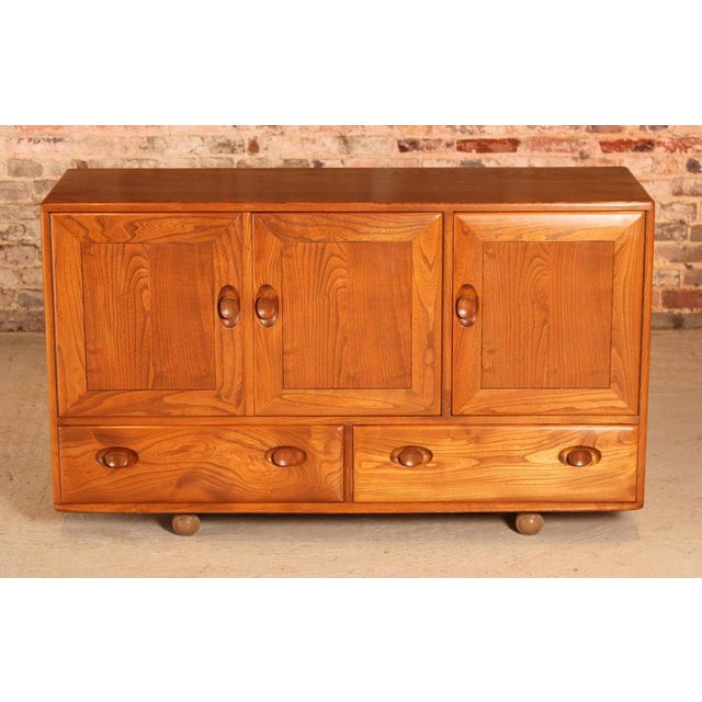 A mid century ercol windsor elm sideboard on casters, circa 1960s. Two drawers, one double doored cupboard and one single...