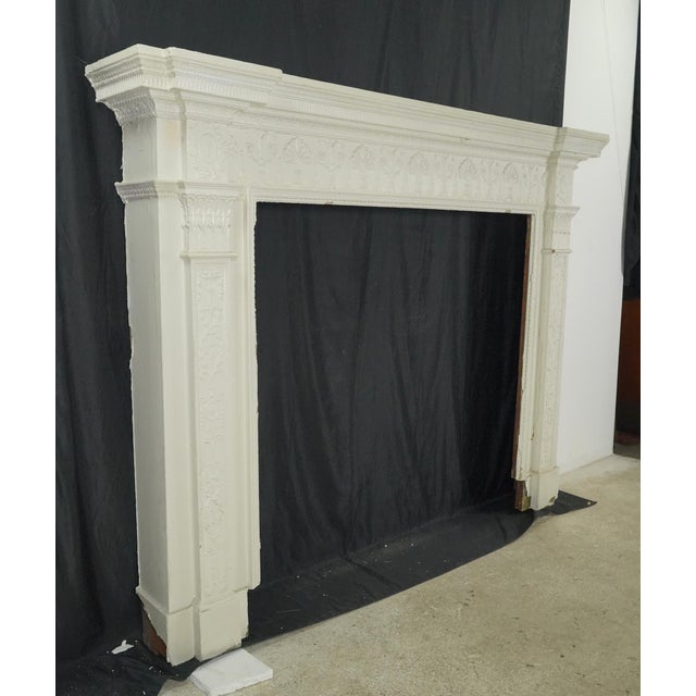 Victorian style fireplace mantel with a thick layer of white paint. It features raised beads, urns, floral, torches, and...