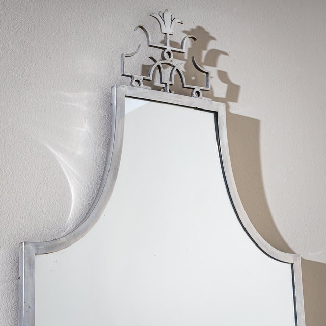 Wall mirror with a simple polished steel frame. The frame rises at the top and is crowned by an ornamental Art Deco crest.