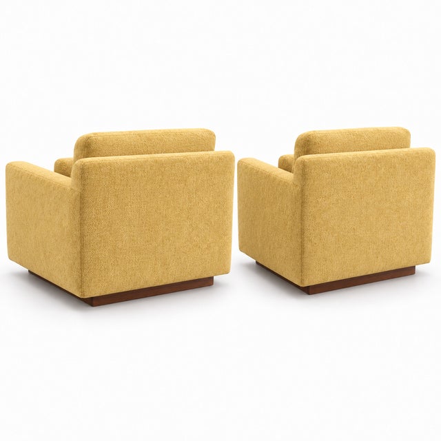 A striking pair of mid-century style lounge chairs upholstered in golden yellow chenille and grounded by rich walnut...