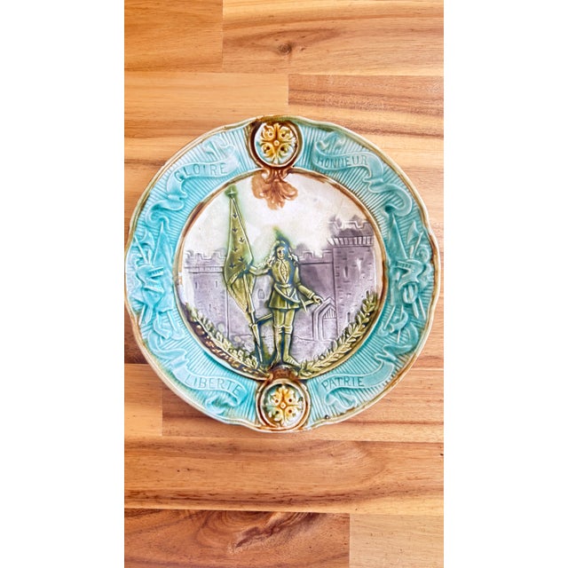 French majolica commemorative plate with relief-molded center depicting Joan of Arc before a fortified tower, holding her...