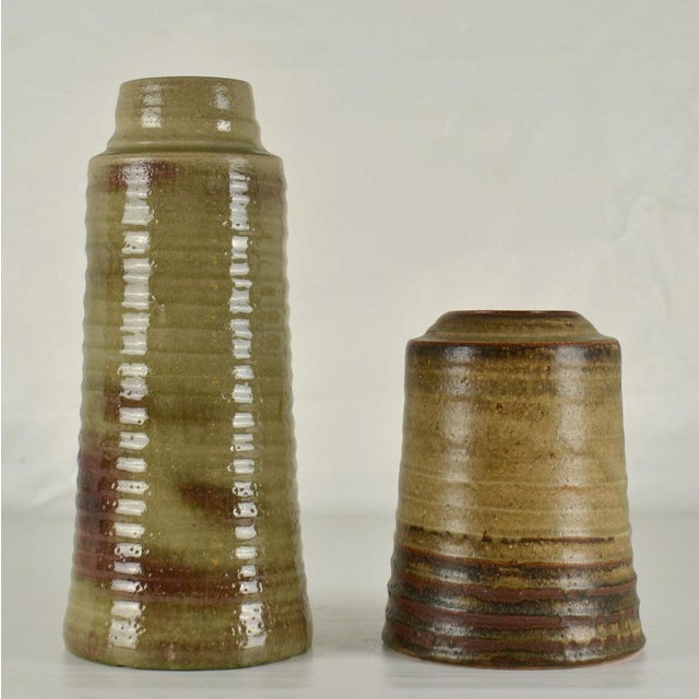 A pair of cylinder vases in differing heights in earth tone glazes in muted tones, created on the turning wheel by highly...