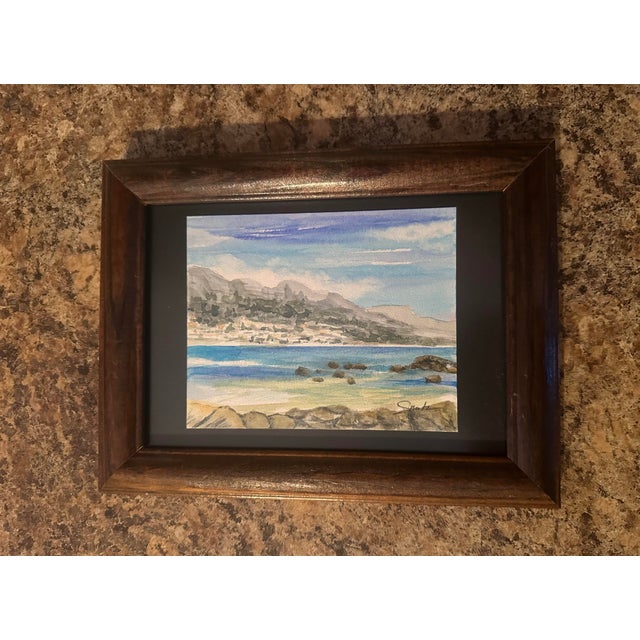 A peaceful seaside landscape capturing the beauty of distant mountains, rolling waves, and rocky shoreline. Gentle blues...