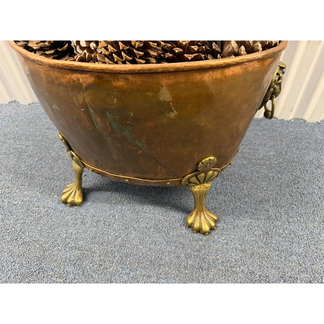 This antique copper and brass kindling holder is a striking hearth accessory featuring ornate lion‑head ring pulls,...