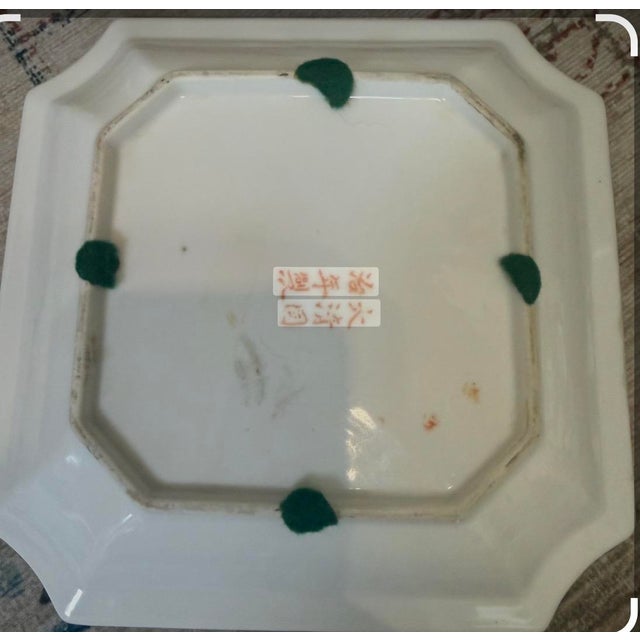 This late 19th-century Chinese porcelain square plate features a distinctive pink glaze and hand-painted "Eight Buddhist...
