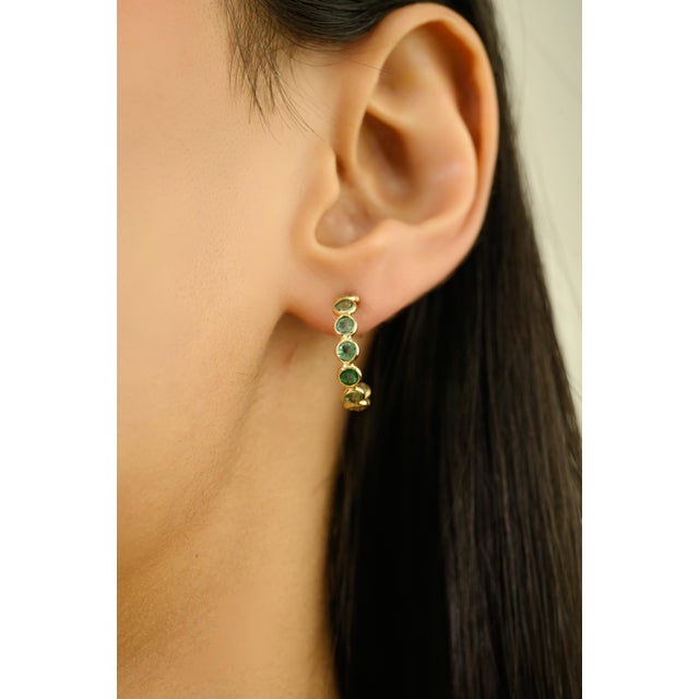 These elegant hoop earrings feature twenty natural round emeralds totaling 2.08 carats, beautifully set in rich 18K yellow...