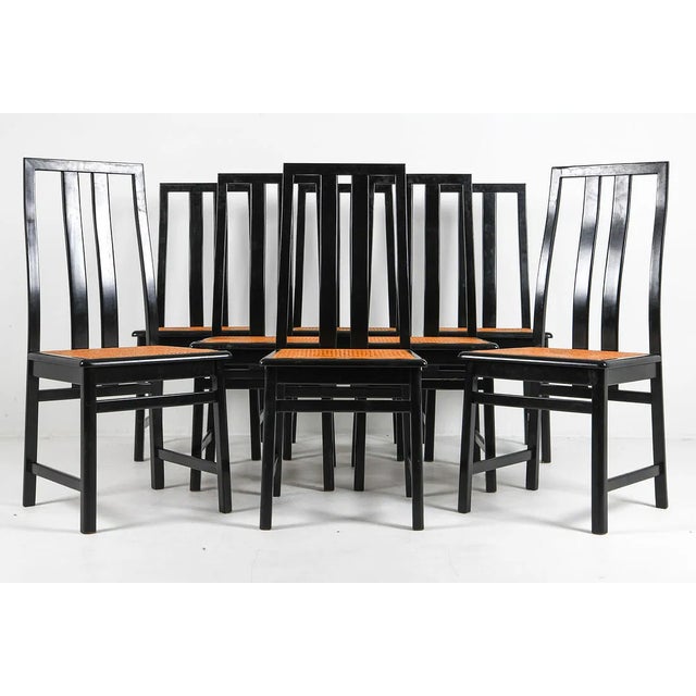 Set of eight dining chairs with black lacquered beechwood frames and woven cane seats. Rectilinear construction with tall...