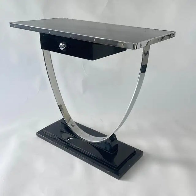 Machine age streamline Art Deco console table rendered in a black lacquered wood base and top supported by a chrome plated...