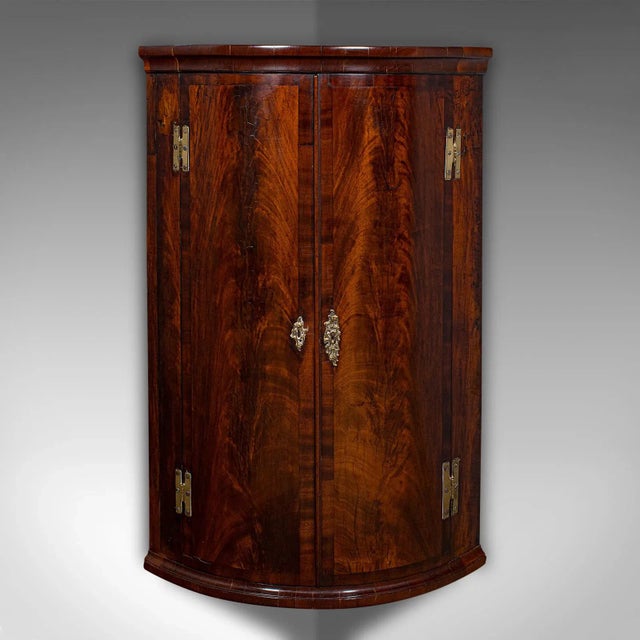 This is an antique bow front corner cabinet. An English, flame mahogany and oak wall cupboard, dating to the mid Georgian...