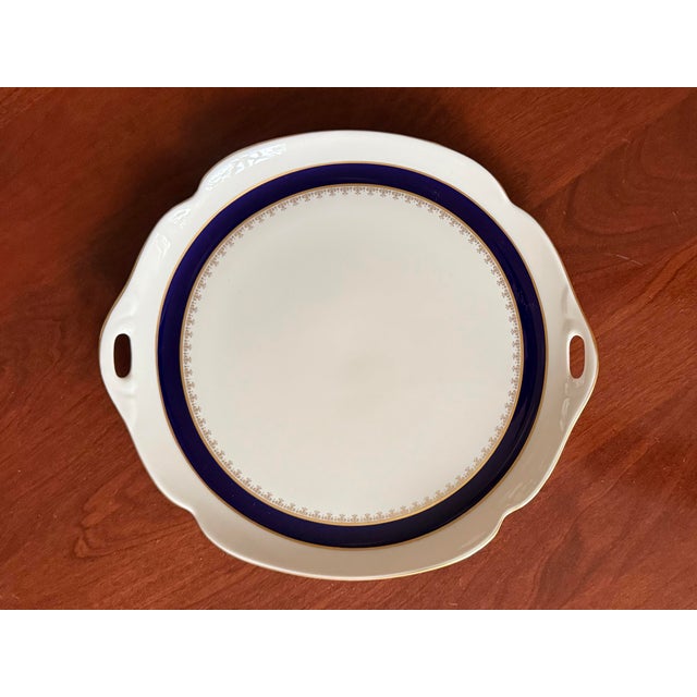 This gorgeous ivory bone china serving plate with cut-out handles features a cobalt blue band and gold filigree design....