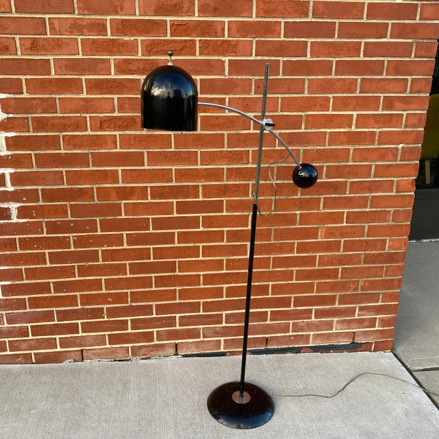 A counterweight floor lamp with an arched horizontal stem landing on a half bell shade. The height setting mechanism is...