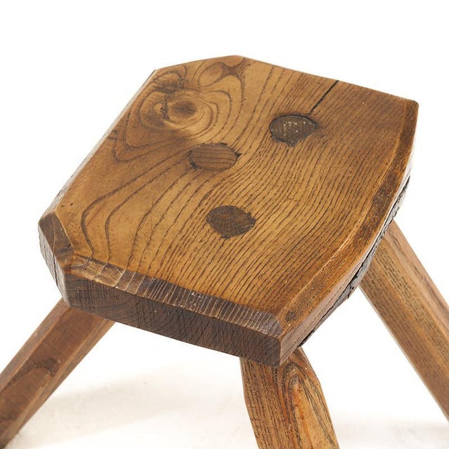Charming Brutalist stool made of solid oak with three legs and a rustic top featuring a beautiful, decorative wood grain....