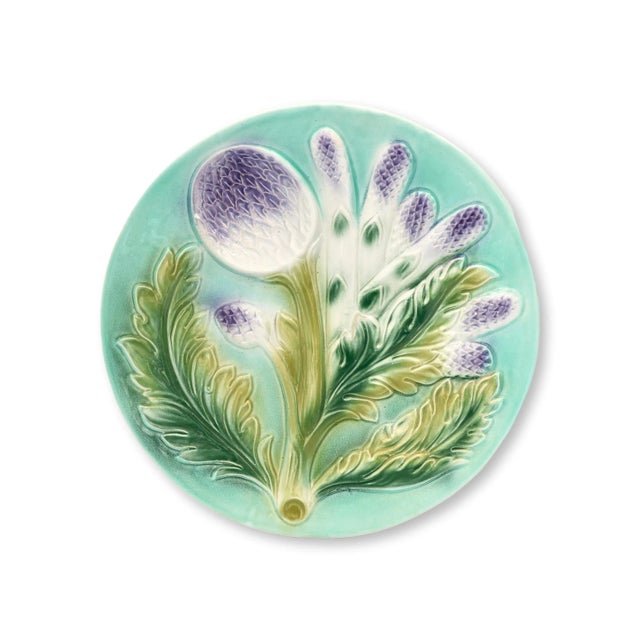 A vibrant set of six majolica plates featuring relief-molded artichokes and asparagus sprays in lavender and green against...