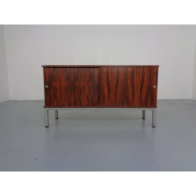 Laminated, small sideboard in rosewood finish by Waiko from the 1970s. Two sliding doors. Behind each door is a large...