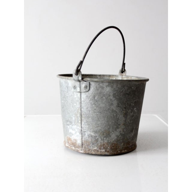 This vintage galvanized metal bucket features a classic utilitarian design with a curved handle for easy carrying....