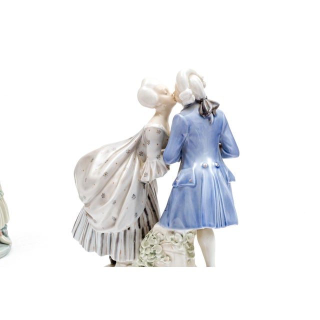 A charming Royal Copenhagen hand-painted porcelain figurine group depicting a Rococo-era courting couple — a gentleman in...