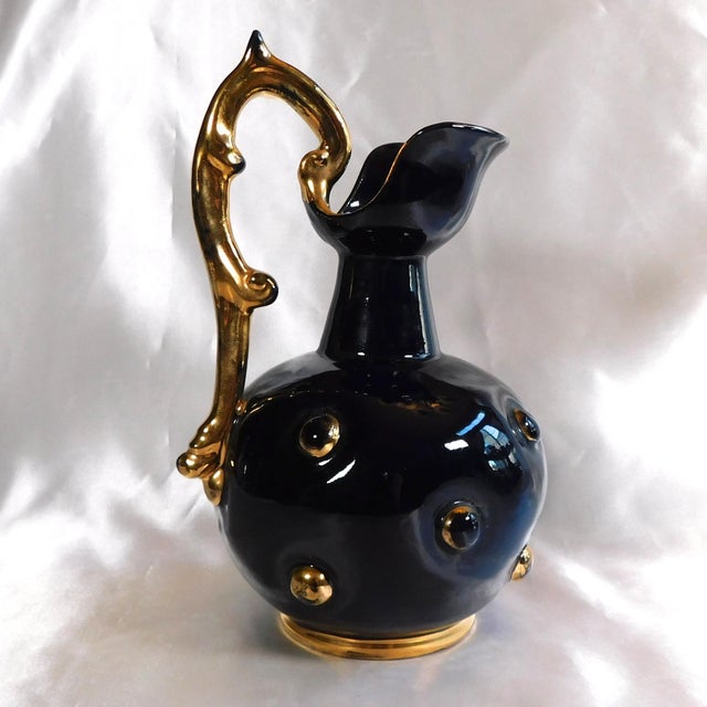 This is a very dark glass pitcher in a dark blue purple. It has indents with glass beads rimmed in gold in the glass plus...