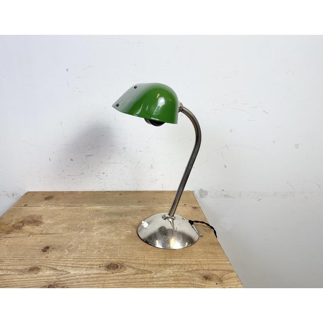 This green table lamp was made in former Czechoslovakia during the 1950s. It features a green enamel shade with a white...