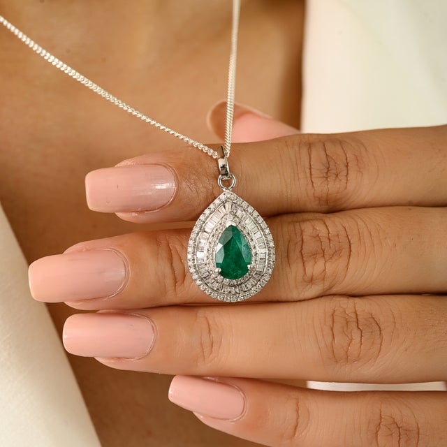 Pear-shaped emerald and diamond halo pendant, finely crafted in 14k white gold. The centerpiece features a vibrant 1.78...