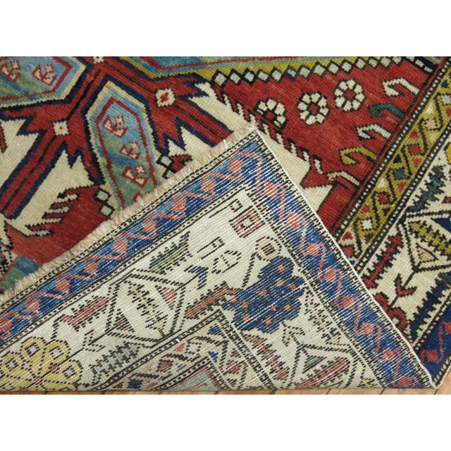 A geometric tribal looking Caucasian shirvan rug from the early 20th century. Brick red field, earth accents in green and...