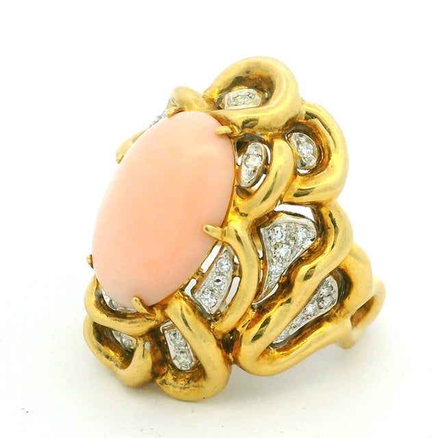 A striking vintage cocktail ring showcasing a beautifully polished oval angel skin coral cabochon set within an elaborate...