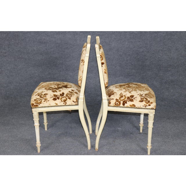 An elegant and beautifully coordinated pair of Louis XVI-style side chairs, distinguished by their finely carved painted...