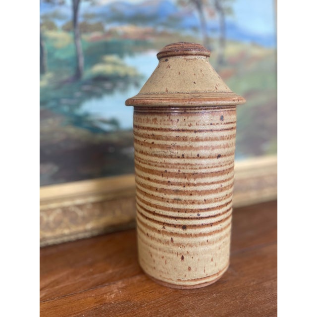 This vintage studio pottery jar features a hand-thrown cylindrical form with a domed, fitted lid. The surface is decorated...