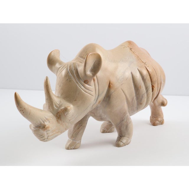 A substantial hand-carved stone rhinoceros sculpture featuring beautiful natural veining and warm, neutral coloration....